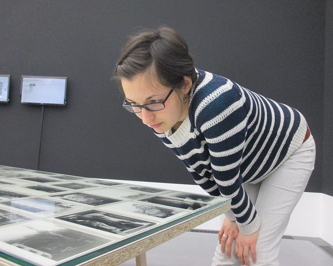 Breinl_Marie Eine Absolventin des Studiengangs Museologie an der HTWK Leipzig betrachtet Fotos, die auf einem Tisch in einer Museumsausstellung liegen.
