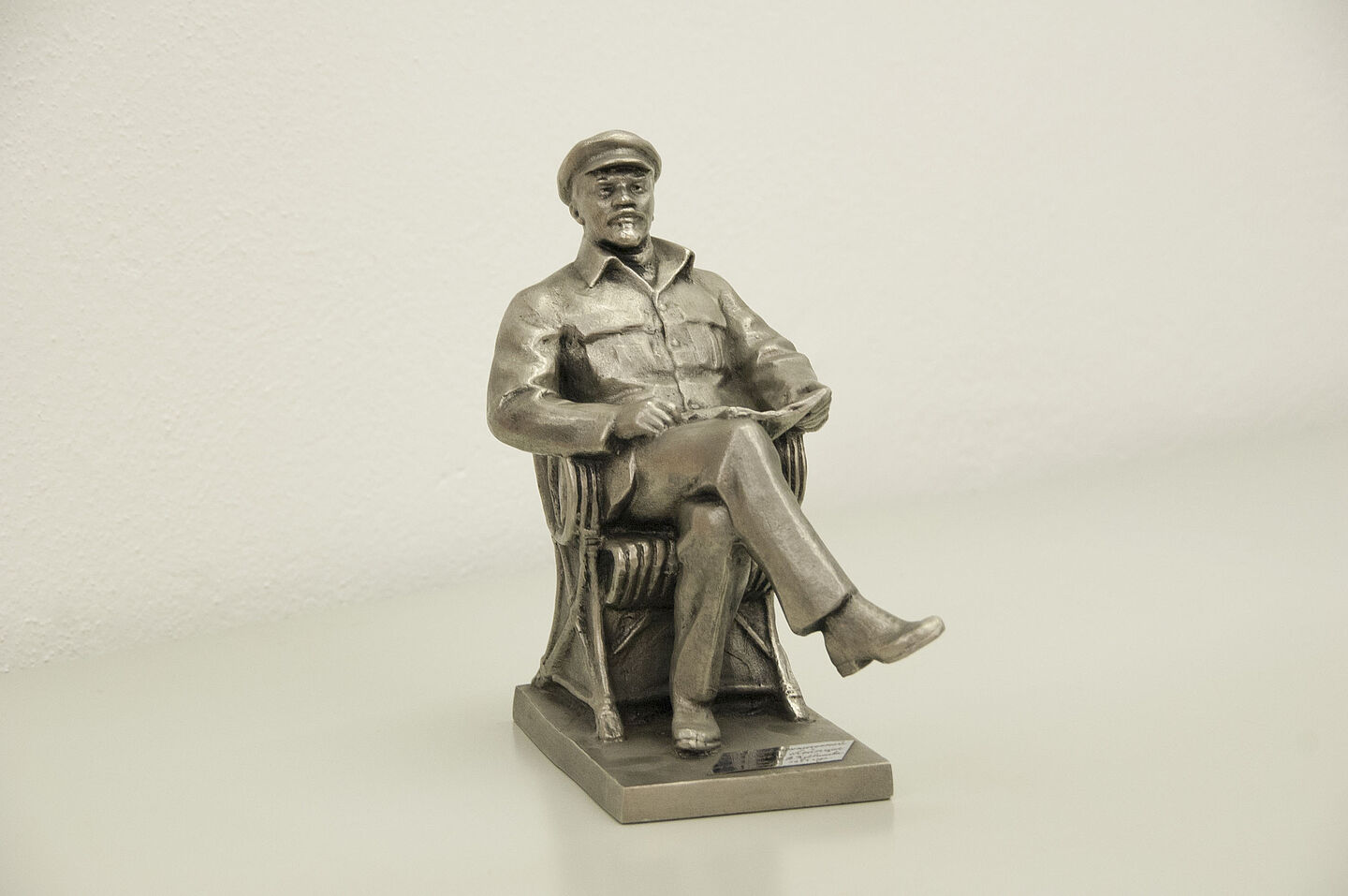 Lenin-Figur aus dem HTWK-Archiv (Foto: HTWK Leipzig) Zu sehen ist eine Eisenfigur von Lenin, der mit überschlagenen Beinen in einem Sessel sitzt, eine Zeitung auf dem Schoß in den Händen hält und leicht nach oben schaut.