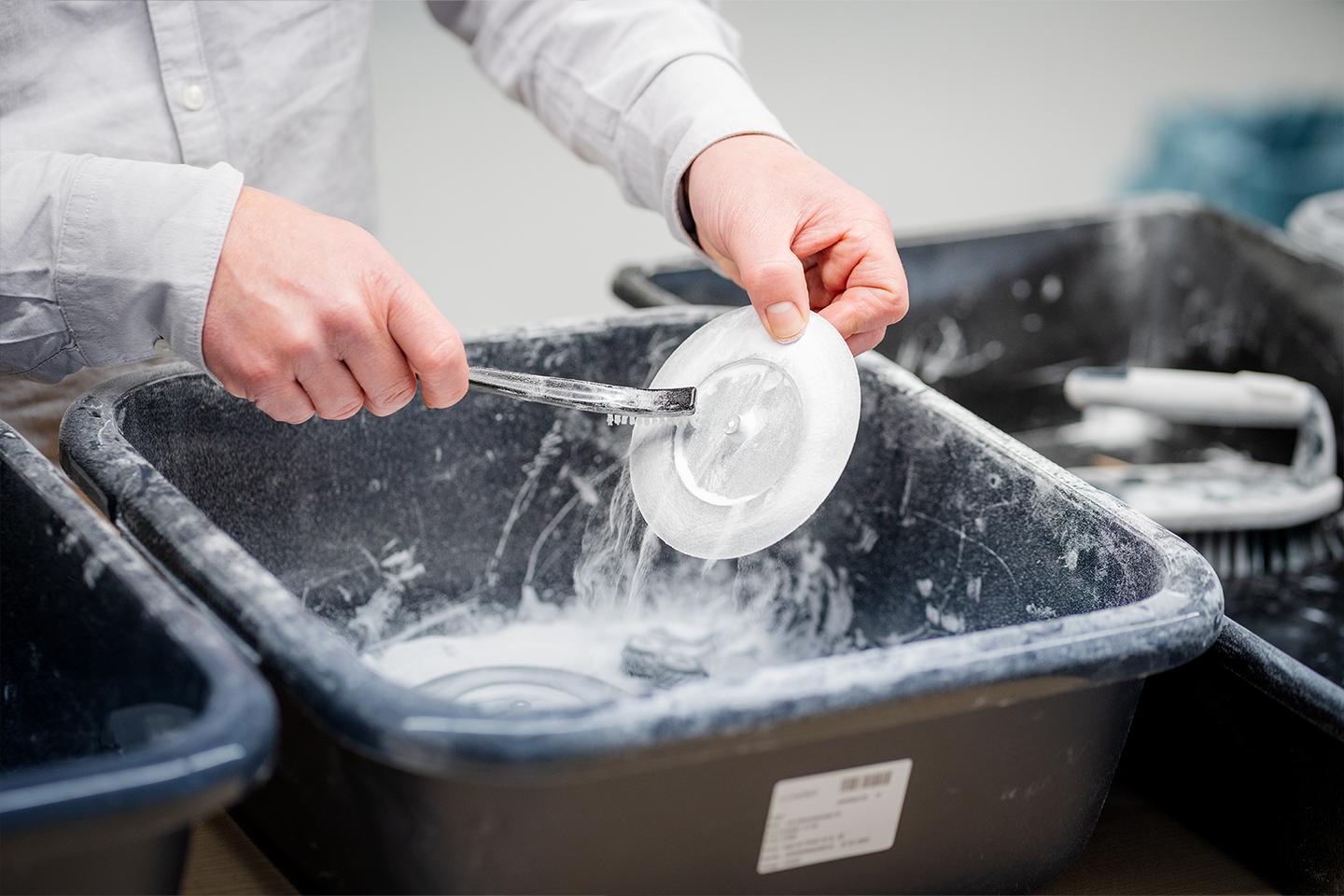 Ein 3D-gedrucktes Bauteil in Form eines kleinen Tellers wird in einer Plastikwanne nass abgebürstet.
