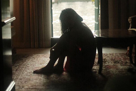 HOME Ein Mädchen sitzt allein auf dem Boden eines dunklen Raumes