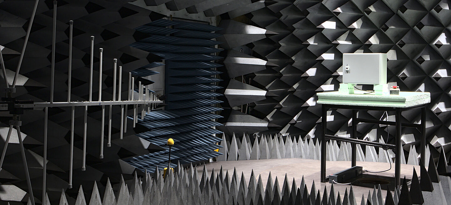 Ein Raum mit spitzen Schallschutzwänden, Messantenne und Gerät auf Tisch