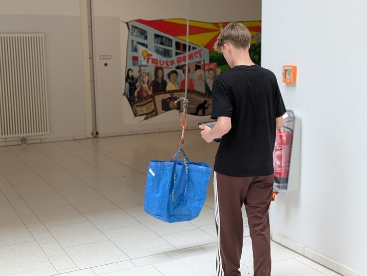 Sport4MINT-Station Aufzug Schüler von hinten im Schulgebäude mit Ikea an herabgelassenem Seil