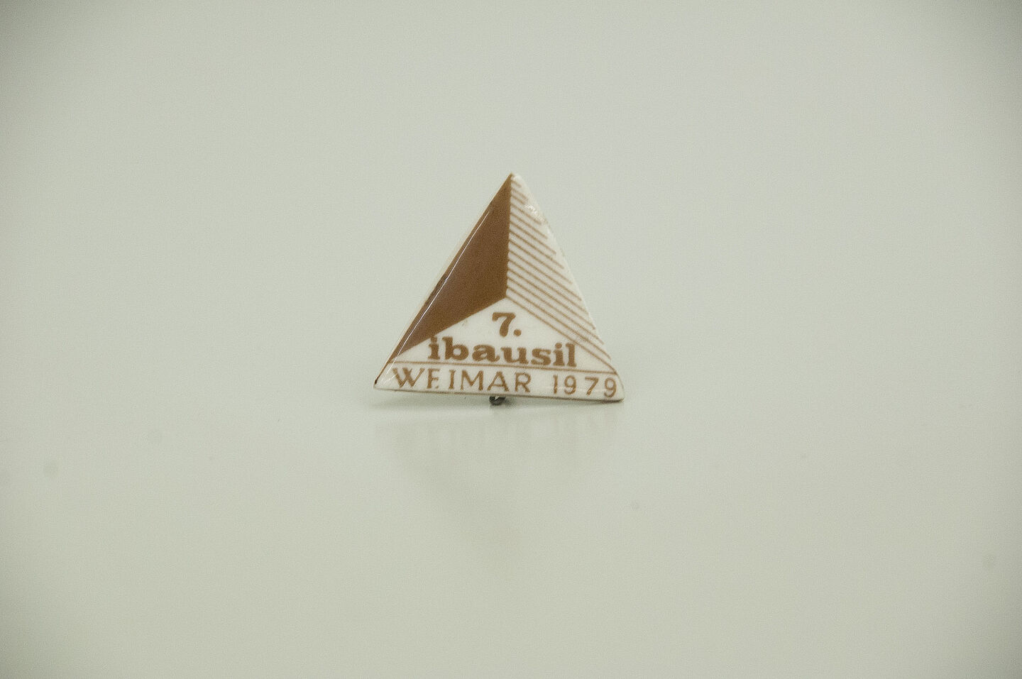 Anstecknadel aus dem HTWK-Archiv (Foto: HTWK Leipzig) Zu sehen ist eine dreieckige Anstecknadel aus Kunststoff, auf der in brauner Schrift steht "7. ibausil Weimar 1979".