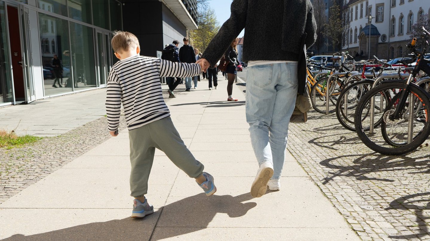 Junge Mutter läuft mit ihrem Kind entspannt am Fechner-Bau der HTWK Leipzig vorbei.