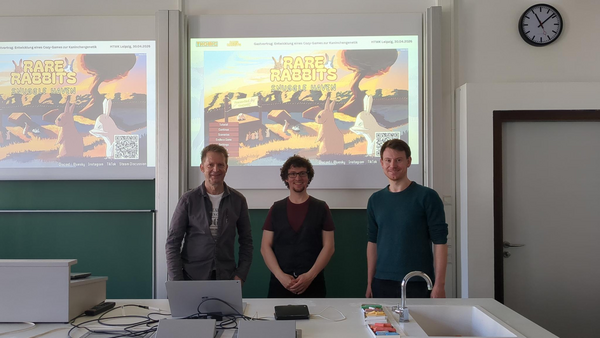 Professor Kulisch, Dr. Nestler und Dr. Graebling stehen im Hörsaal und im Hintergrund ist die Präsentation zu sehen.