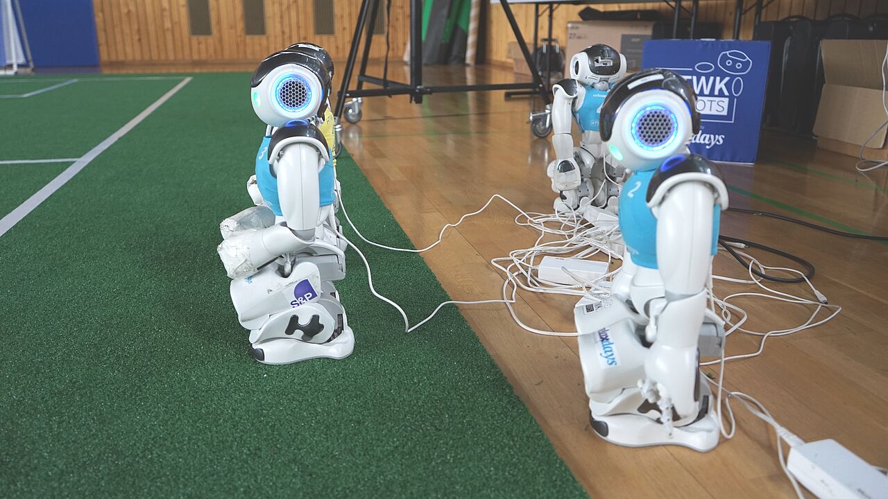 drei humanoide Fußball-Roboter am Ladekabel