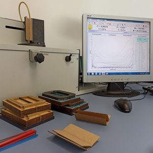 Messgerät mit Wellpappeproben und angezeigten Kurvendiagrammen am Monitor