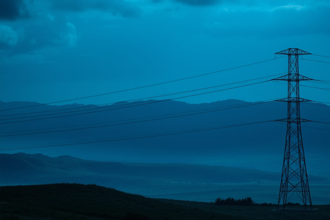 Strommast in hügeliger Landschaft bei blauem Abendlicht