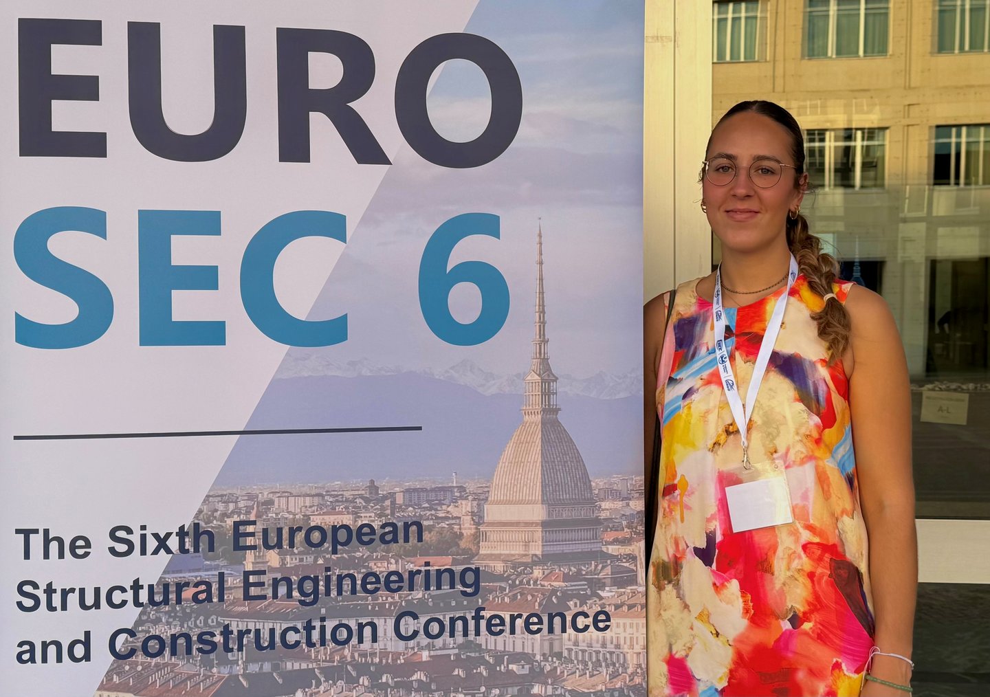 Sixth European Structural Engineering and Construction Conference Doktorandin steht neben Werbeplakat der Tagung
