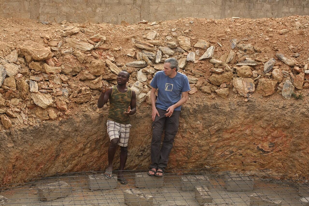 Ein deutscher und ein togolesischer Mitarbeiter stehen in der ausgehobenen Grube und beraten zum bevorstehenden Bau.