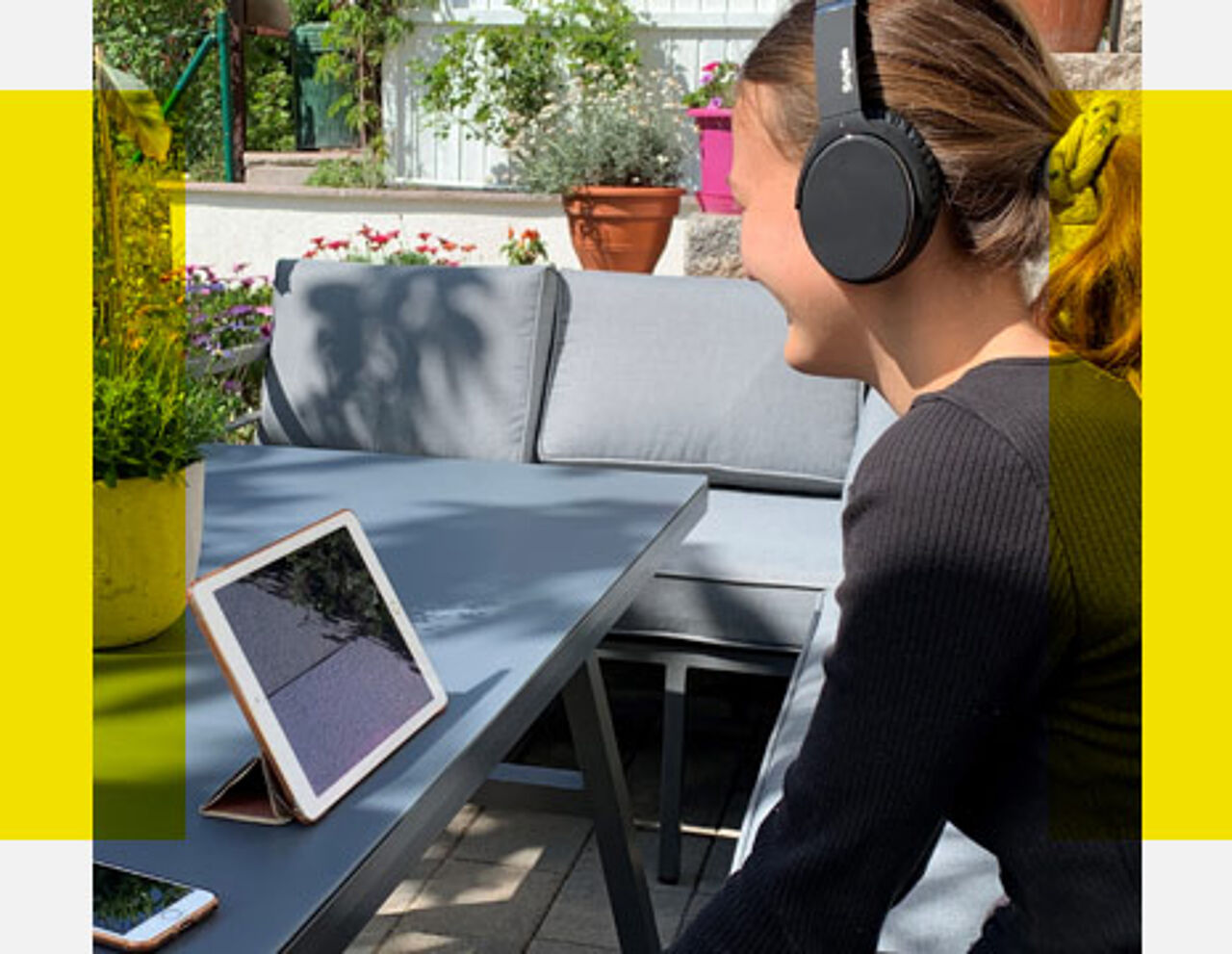 Eine Junge Frau sitzt mit Kopfhörern auf der Terrasse vor einem Monitor und nutzt die Online-Studienorientierungswerkzeuge der HTWK Leipzig. 