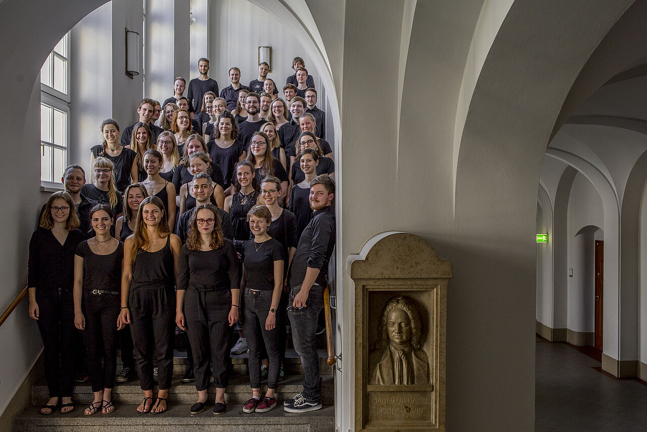 Das HTWK Orchester steht auf einer Treppe im Geutebrückbau. Alle sind in schwarz gekleidet.