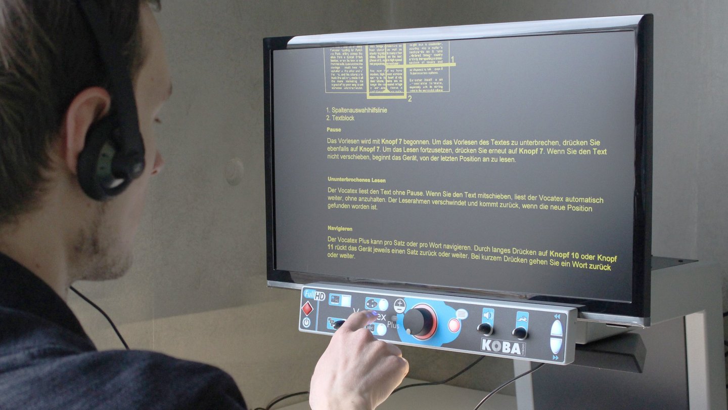 Arbeitsplatz mit Vergrößerung und Vorlesesystem für Printmedien Nutzer mit Kopfhörern bedient das Vorlesesystem an einem Bildschirm in der Hochschulbibliothek
