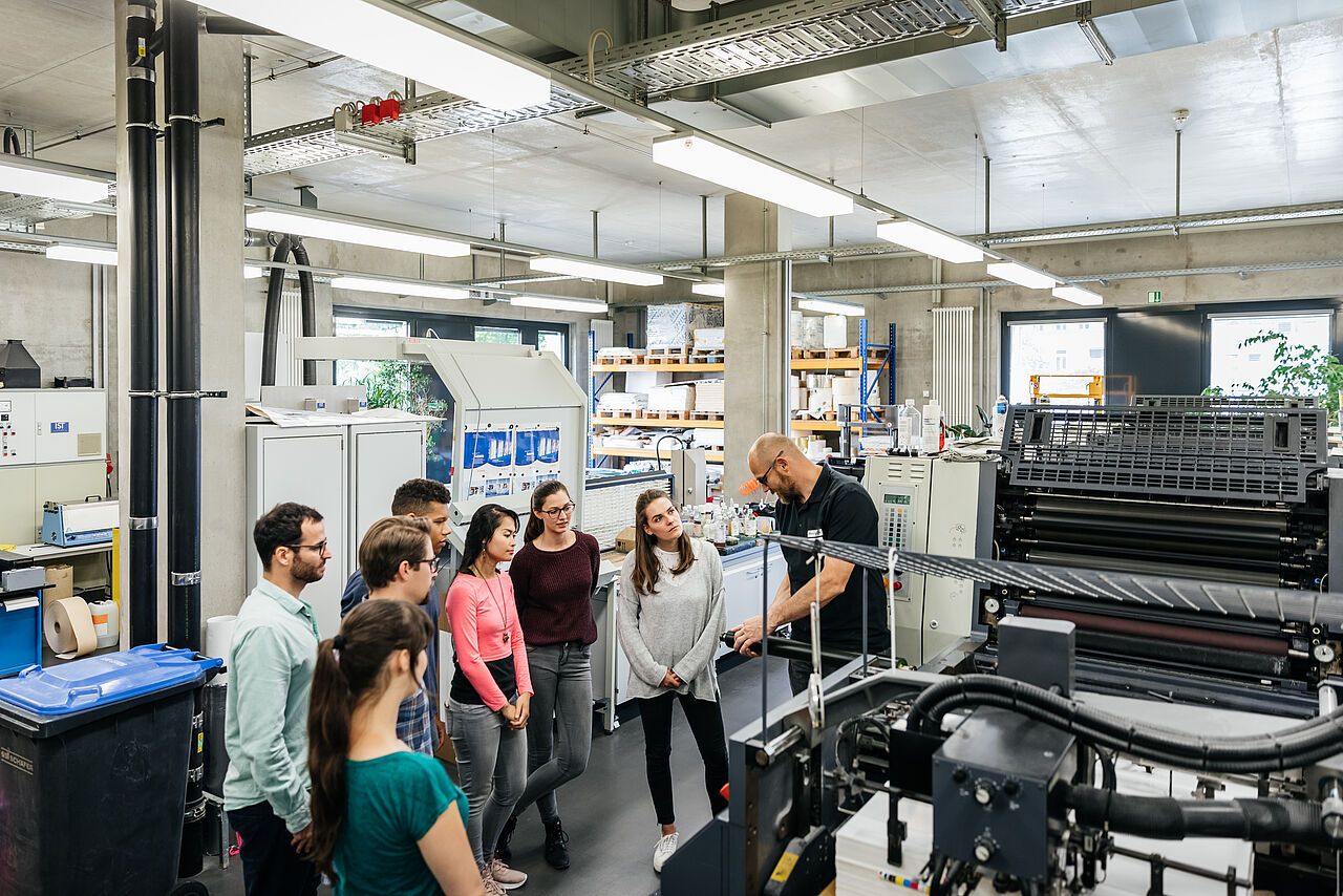 A professor explains a machine in the print room to a group of students
