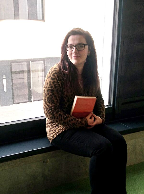 Ariane Lösch sitzt auf einer Fensterbank und hält ein geschlossenes Lehrbuch im Arm.