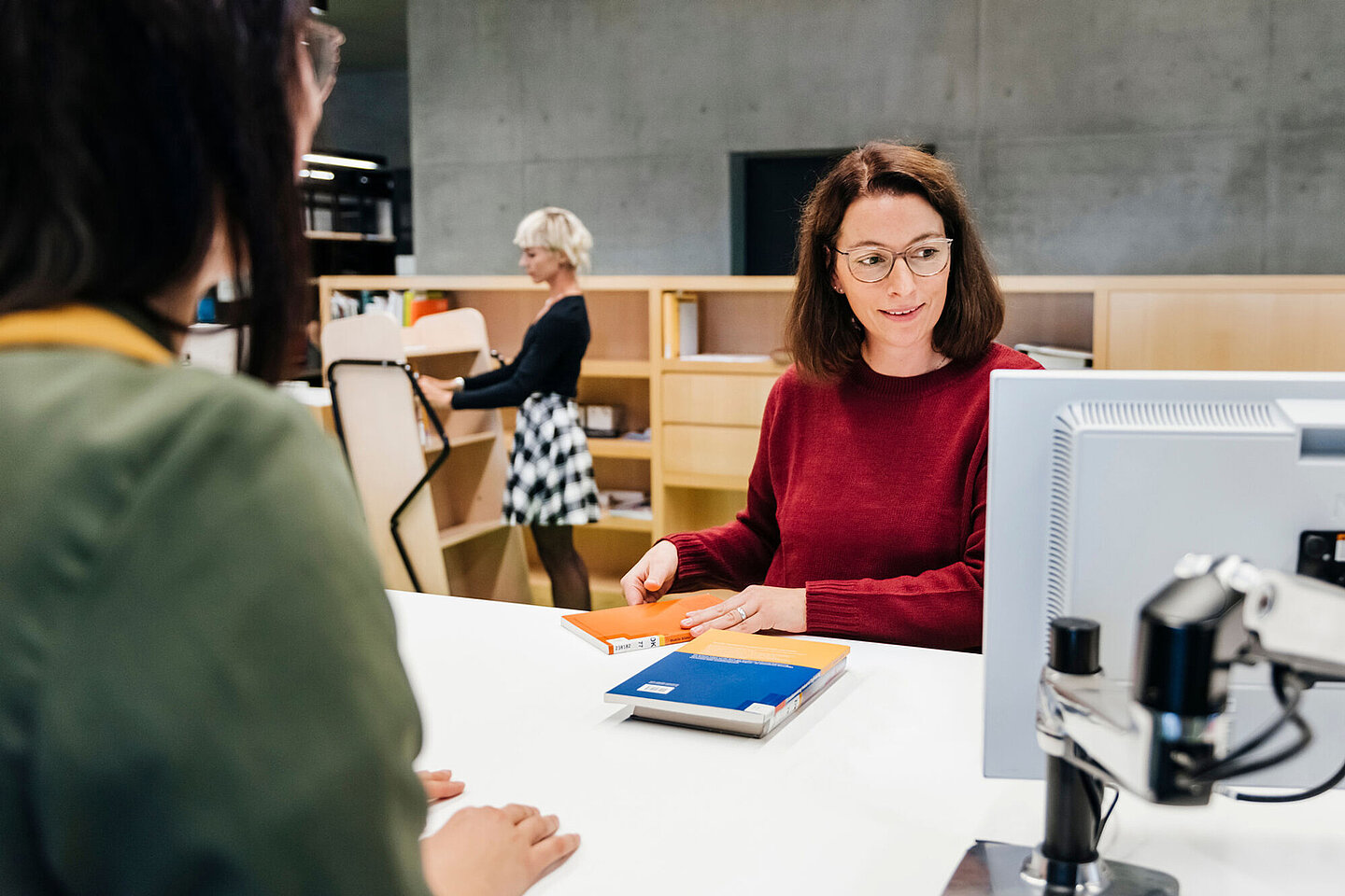 Eine Studentin am Empfangstresen der Hochschulbibliothek wird von einer Mitarbeiterin bedient.
