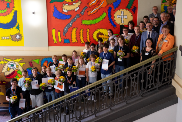 Die Siegerinnen und Sieger des diesjährigens sachsenweiten Informatikwettbewerbs. eine große Gruppe von Kindern und wenigen Erwachsenen steht auf einer Treppe in einem buntbemalten Treppenhaus