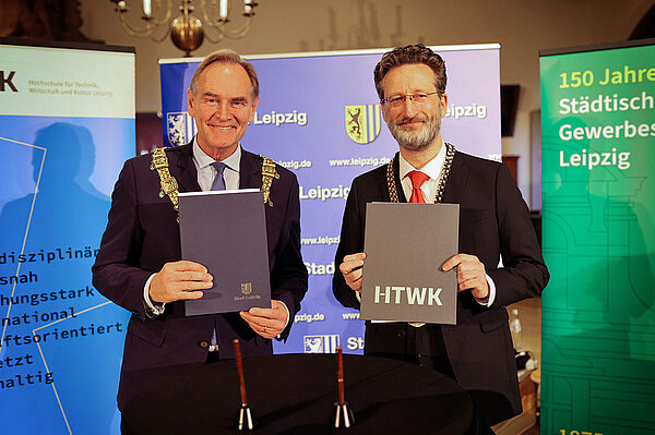 zwei Herren haltne je eine festliche Urkundenmappe in die Kamera