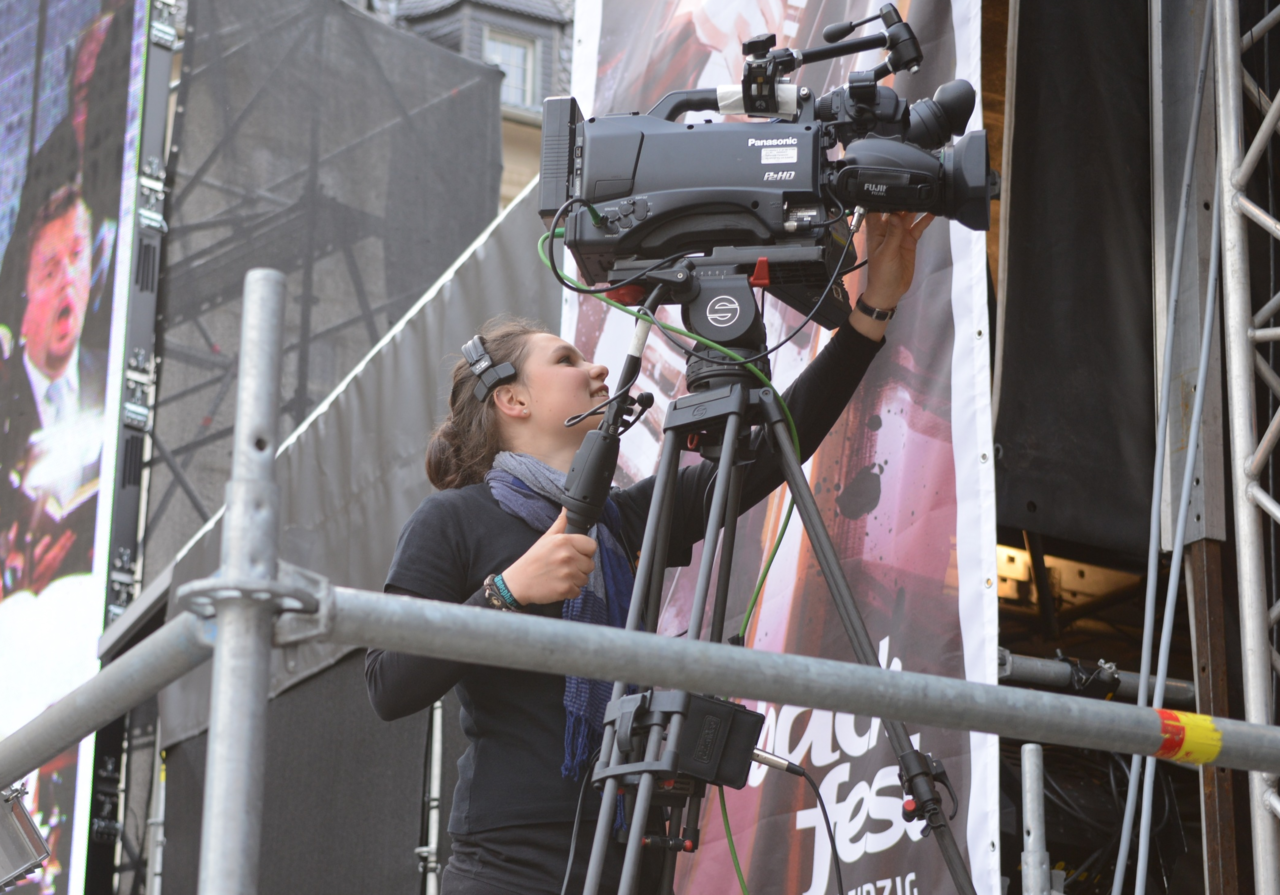 Ein Mädchen steht hinter einer Kamera und filmt bei einer Openair-Show das Geschehen auf der Bühne.