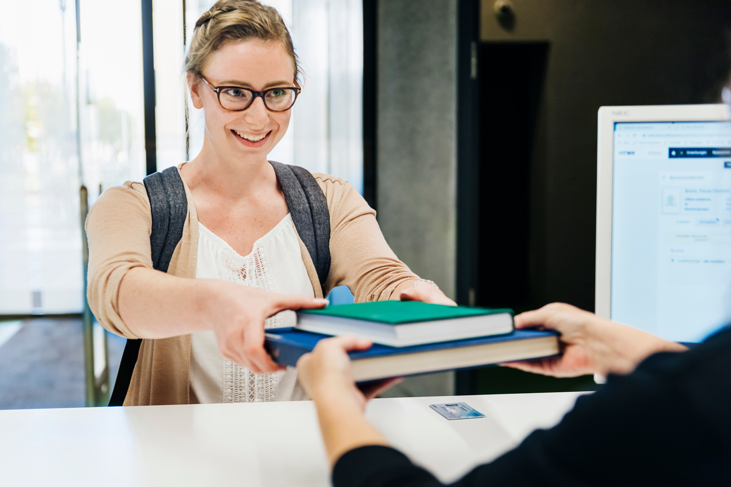 Bücher ausleihen Studierende gibt zwei Bücher am Schalter der Bibliothek zurück.