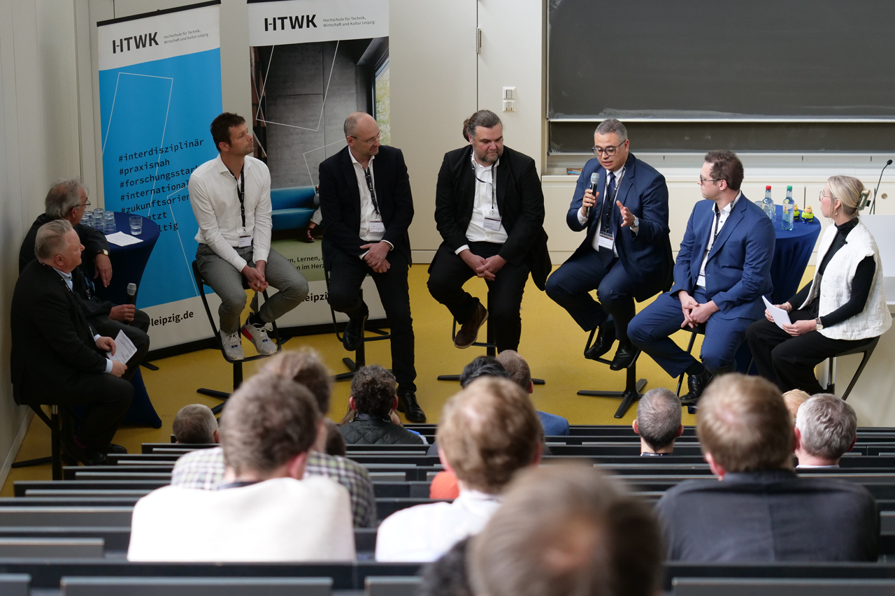 Personen einer Podiumsdiskussion sitzen im Halbkreis im Hörsaal und diskutieren