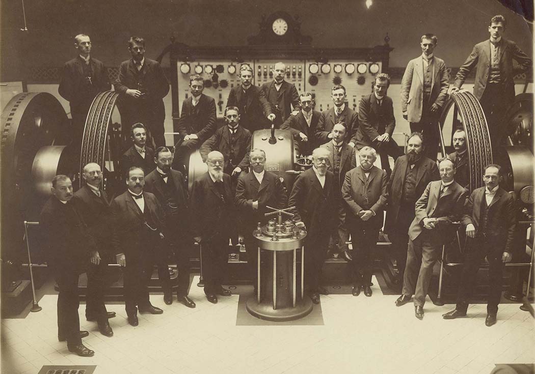 Around 20 male students and lecturers pose in a machine shop