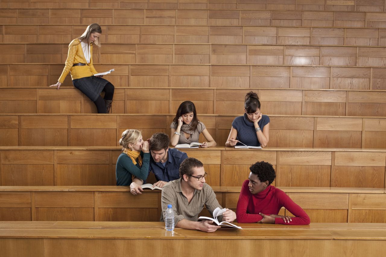A few students sit in a lecture hall and talk to each other