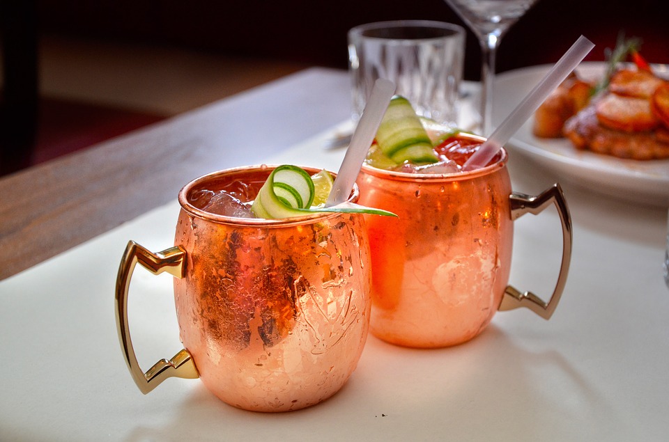 Two cocktails in bronze cups with ice and cucumber