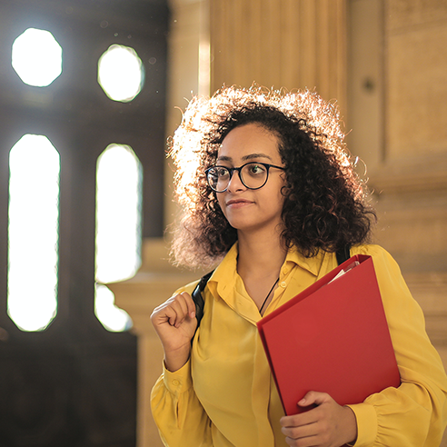 Eine Studentin hält eine rote Mappe in der Hand und schaut in die Ferne.