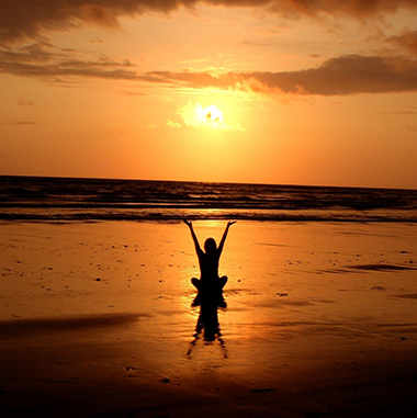 Eine Frau meditiert bei Sonnenuntergang an einem Strand.