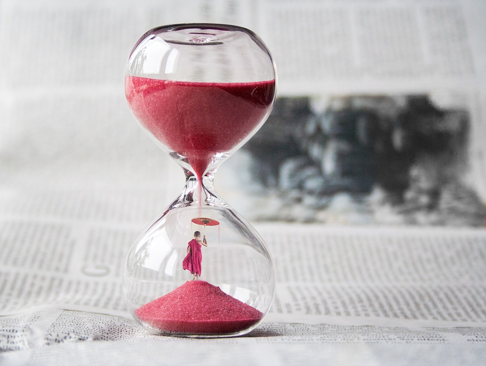 Es ist eine Sanduhr mit rotem Sand zu sehen. Dieser rieselt vom oberen Gefäß in die untere Rundung.