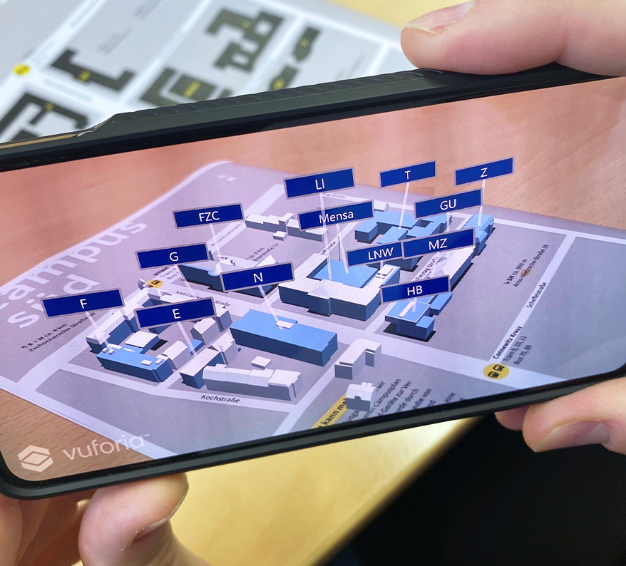 Foto eines Smartphones, auf dem man einen dreidimensionalen Campusplan sehen kann - dieser wird mittels Augmented Reality angezeigt, wenn man sie Rückseite des Reports scannt