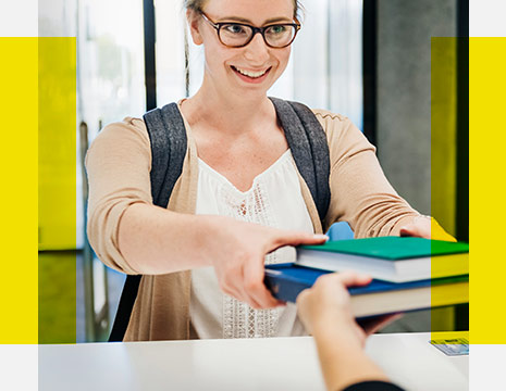Eine junge Frau erhält Bücher aus der Bibliothek und lächelt.