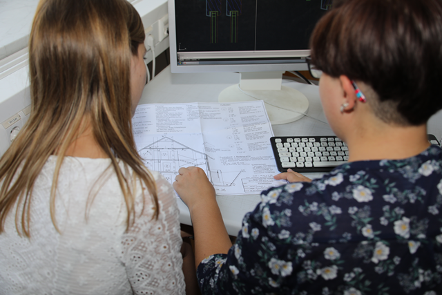 Schnittbild von zwei Studierenden an einem Tisch, die einen Konstruktionsplan anschauen.