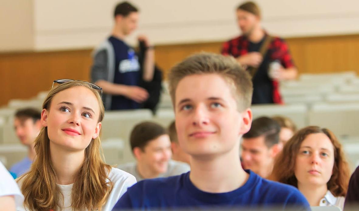 Mehrere Studierende sitzen in einem Vorlesungssaal und hören dem Dozierenden zu.