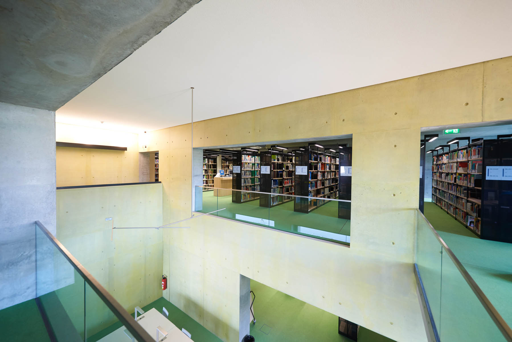 Innenansicht der Bibliothek über zwei Etagen. Im unteren Bereich finden sich Arbeitsplätze zum Selbststudium und in der oberen Etage Bücherregale mit Leihexemplaren.