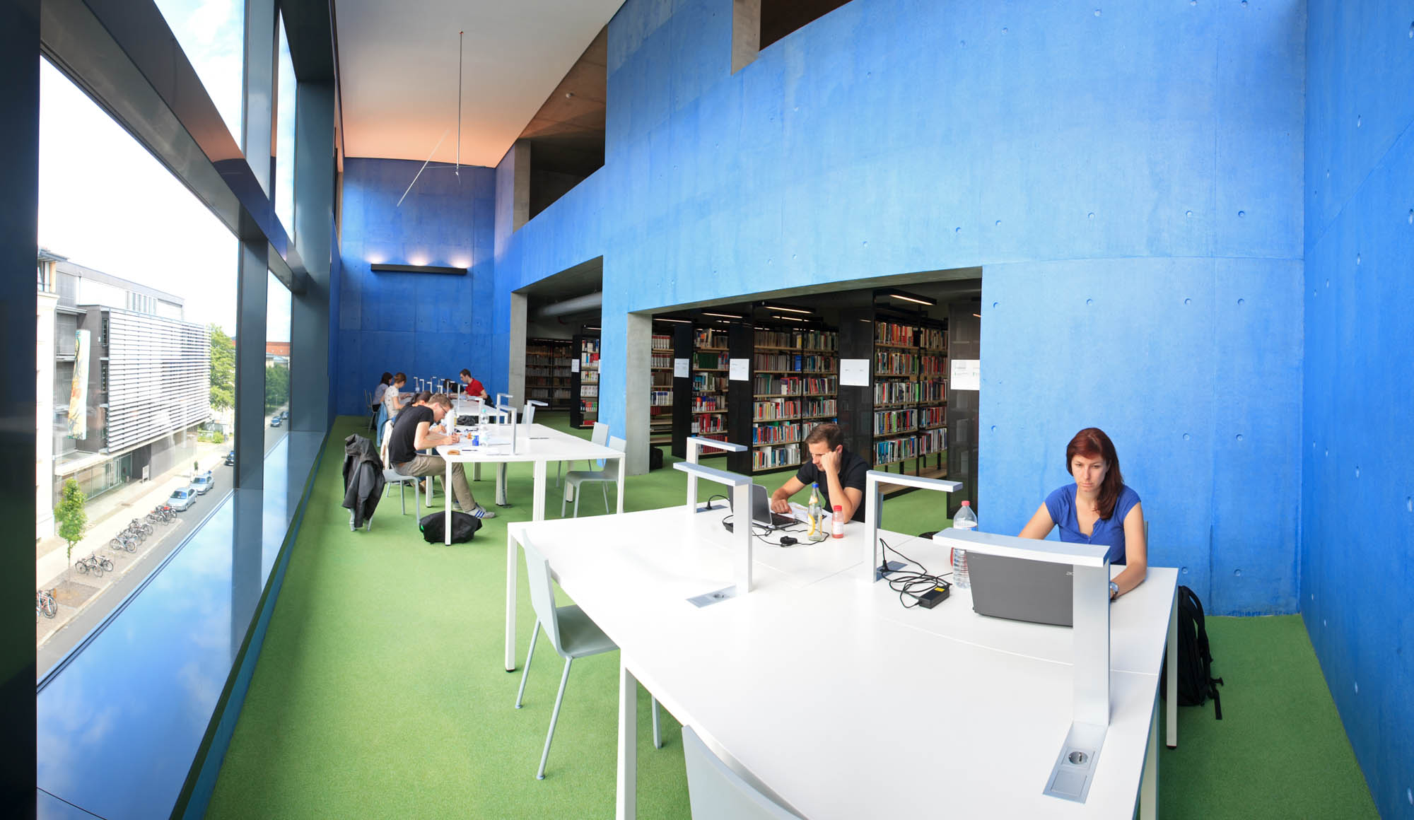 In der Hochschulbibliothek der HTWK Leipzig sitzen mehrere Studenten am Schreibtisch und arbeiten am Laoptop. Im Hintergrund sieht man Bücherregale.