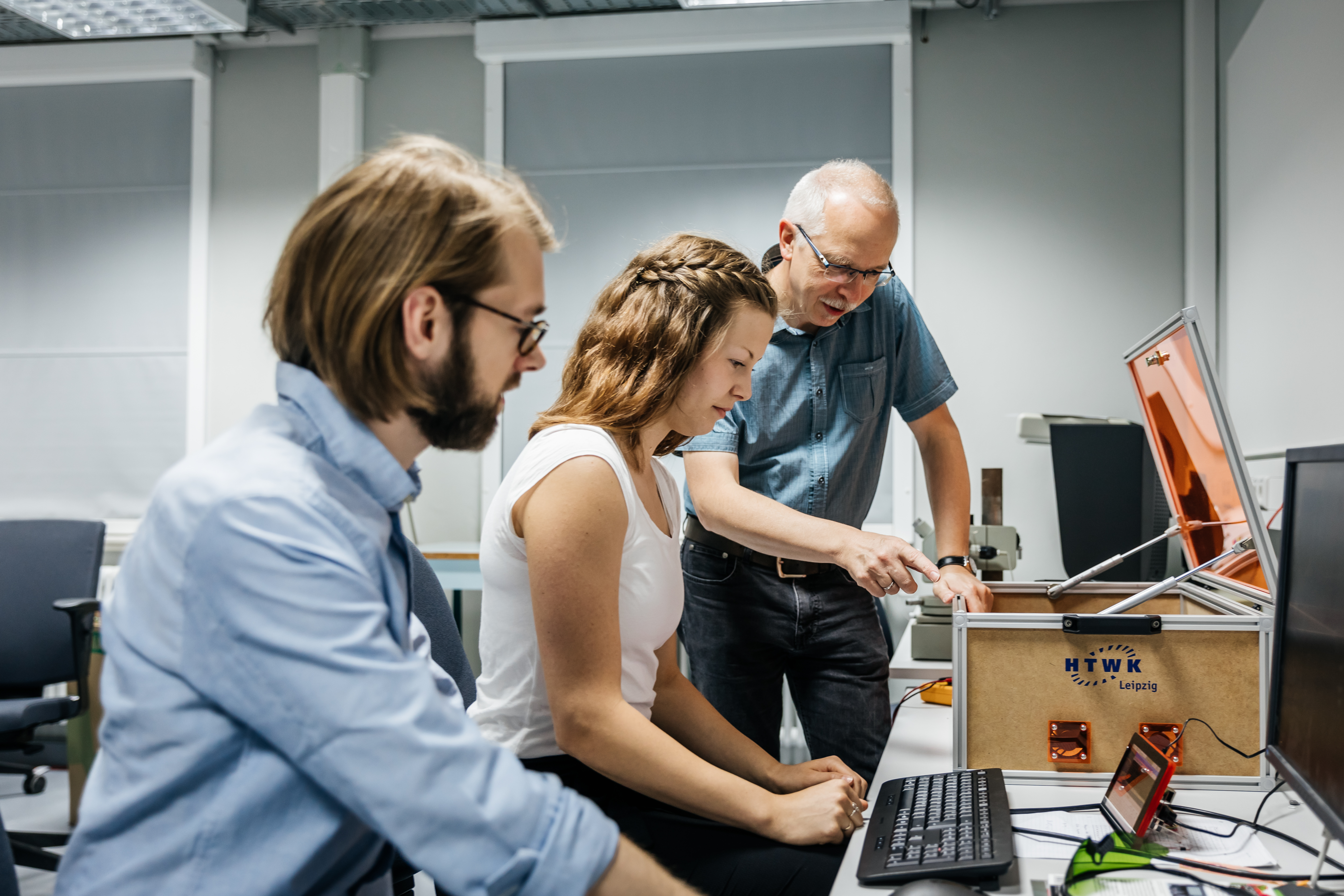 Zwei Studierende und ein Professor betrachten gemeinsam einen Druckprozess.