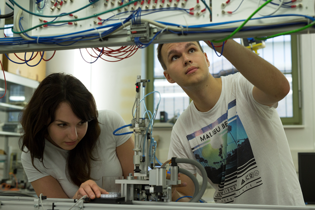 Frontalaufnahme von zwei Studierenden, die sich mit elektrotechnischen Apparaturen im Labor beschäftigen.