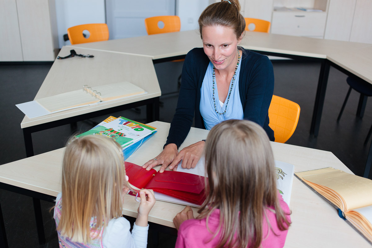 Dr. Julia Dobroschke zeigt zwei Kindern ein Buch in Brailleschrift.